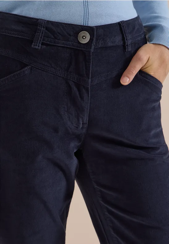 Pantalon en velours côtelé bleu marine, bouton apparent, coutures visibles et main dans la poche.