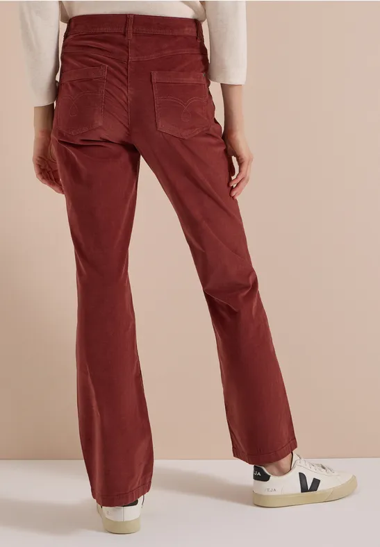Pantalon en velours côtelé rouge à coupe ample, poches arrière, porté avec des baskets blanches sur fond neutre.