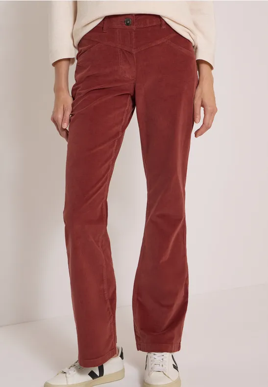 Pantalon en velours côtelé rouge rouille, coupe droite, porté avec des baskets blanches.