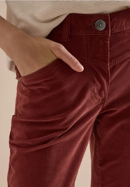 Gros plan sur un pantalon en velours côtelé rouge-brun avec une main dans la poche.
