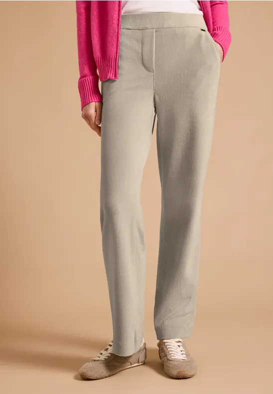 Pantalon de survêtement beige avec poches, baskets claires et haut rose sur fond neutre.