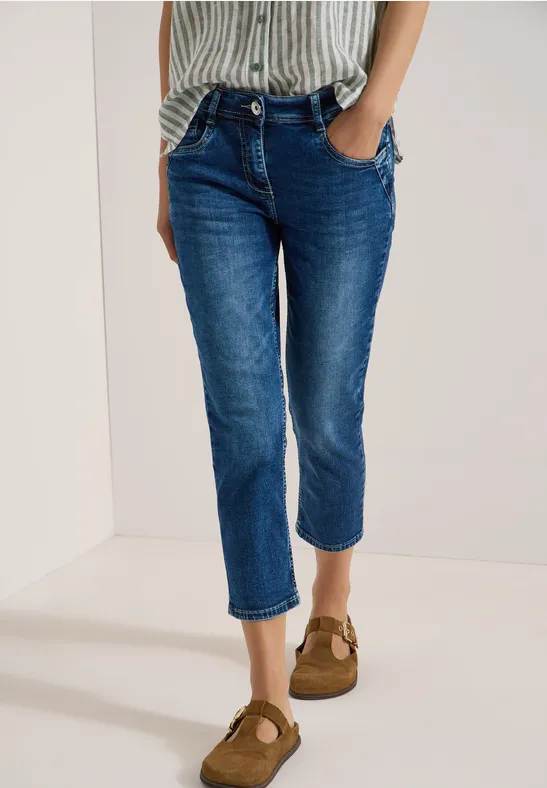 Een persoon draagt donkerblauwe enkeljeans en bruine platte schoenen.