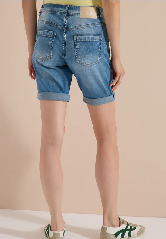 Frau von hinten in hellblauen, umgeschlagenen Jeans-Shorts, gelbem Top und weißen Sneakers.