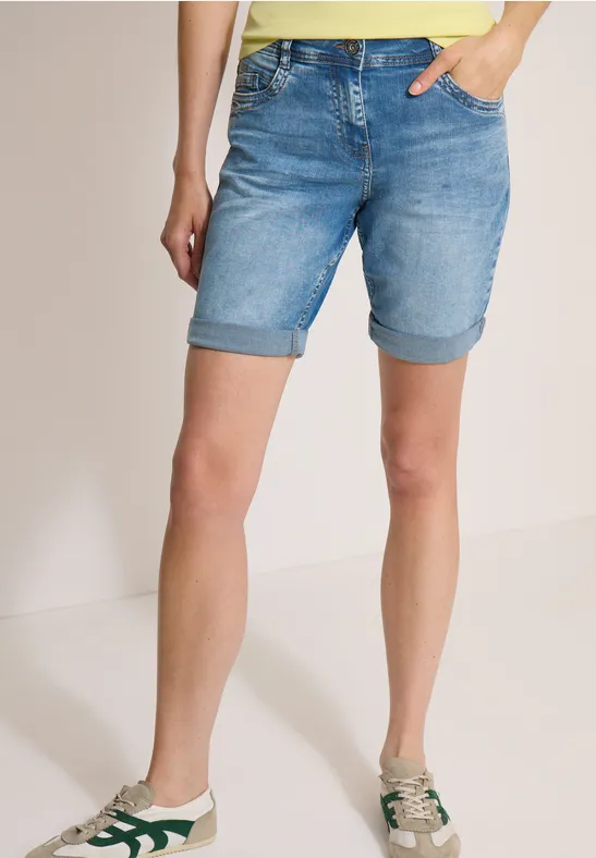 Eine Frau trägt hellblaue, aufgekrempelte Jeans-Shorts und weiße Sneaker mit grünen Details.