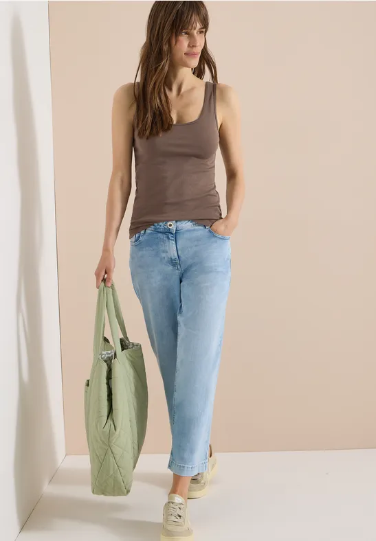 Frau in braunem Top und Jeans trägt grünen Stoffbeutel.