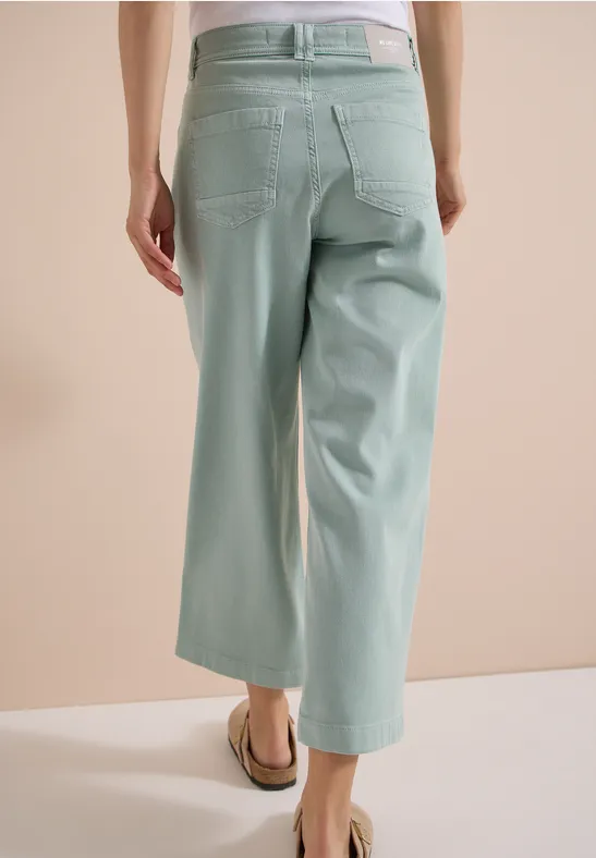 Achteraanzicht van model met pastelgroene, wijdvallende 7/8-broek en platte sandalen.