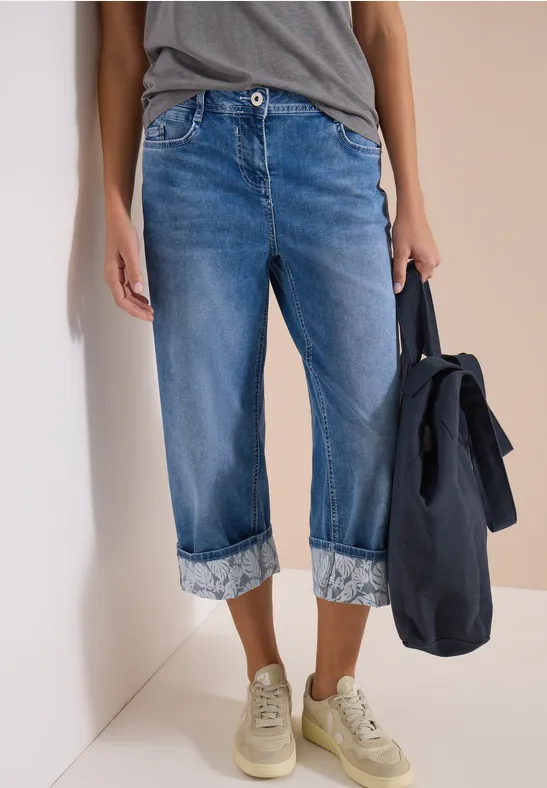 Hochgekrempelte Jeans, lässiges T-Shirt, Sneaker und Tasche in der Hand.