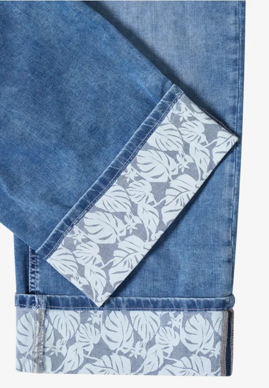 Blaue Jeansbeine mit umgeschlagenem Saum, der ein weißes Blumenmuster zeigt.