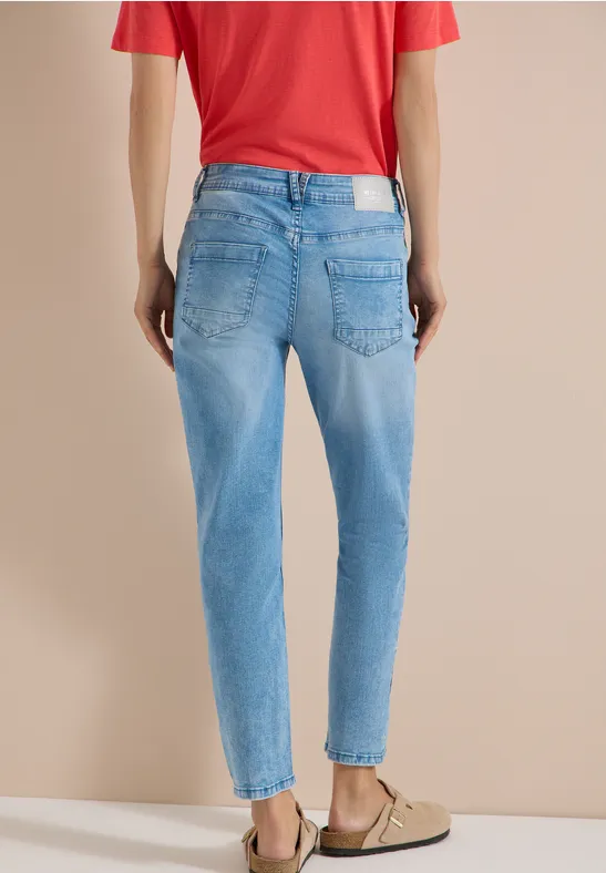 Person steht von hinten, trägt helle, taillierte Jeans mit hohem Bund, rotes Shirt und beige Mules.