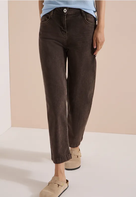 Eine Person trägt schwarze, hoch sitzende Jeans und helle bequeme Schuhe vor neutralem Hintergrund.