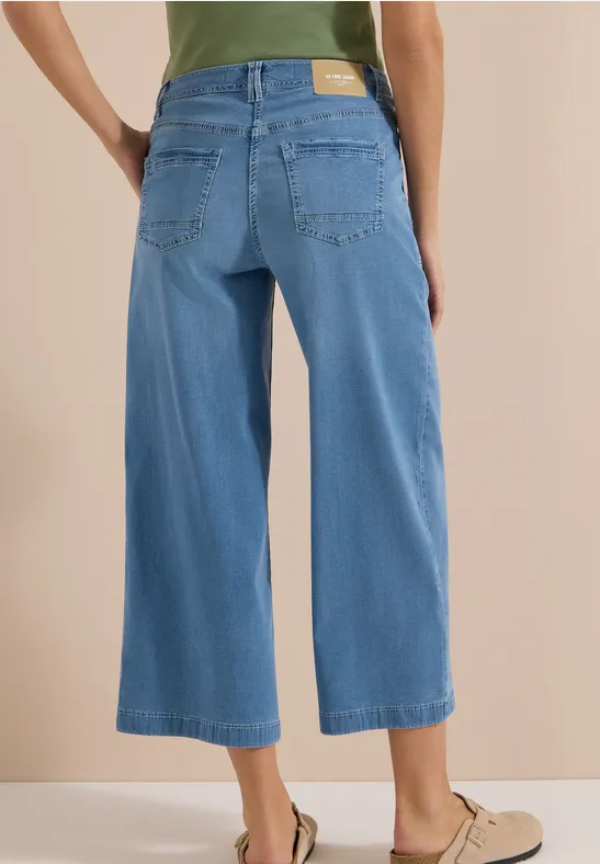 Femme de dos portant un jean culotte clair, taille haute, longueur cheville, associé à des slippers beige.