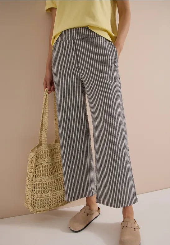 Femme en pantalon ample rayé gris, haut jaune, sac en osier et mocassins beiges.