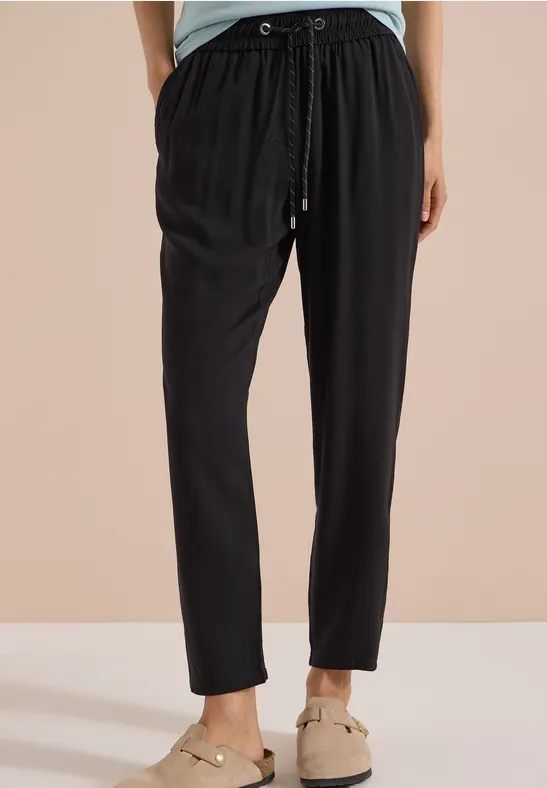 Schwarze, locker sitzende Hose mit Kordelzug an der Taille, kombiniert mit beigen Slippern.
