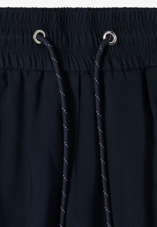 Gros plan d'une ceinture de pantalon bleu marine élastique, cordon noir à pois blancs et œillets métalliques.