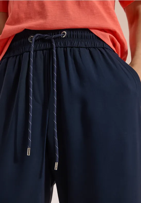 Plan rapproché d'un pantalon bleu marine à cordon de serrage porté avec un haut rouge.