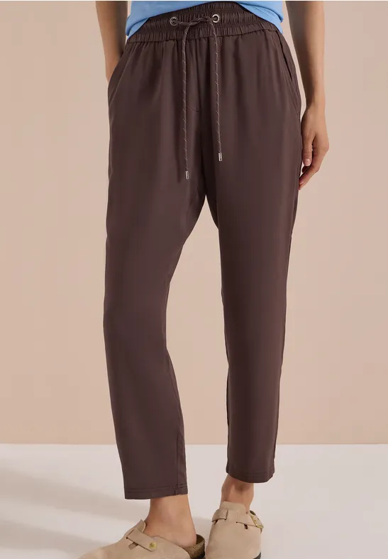 Damenhose aus braunem, leichtem Stoff mit Gummibund und Kordel sowie schmal zulaufenden Beinen.