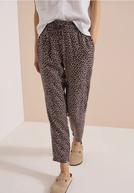 Ein Modell trägt eine locker sitzende schwarze Hose mit weißem Tupfenmuster, weiße Bluse und beige Slipper.