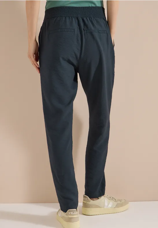 Donkerblauwe joggingbroek gezien van achteren, elastische taille, taps toelopende pijpen, met lichte sneakers.