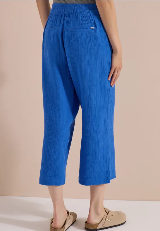 Blaue, plissierte 7/8-Hose mit elastischem Bund, weit geschnitten, kombiniert mit beigen Sandalen.