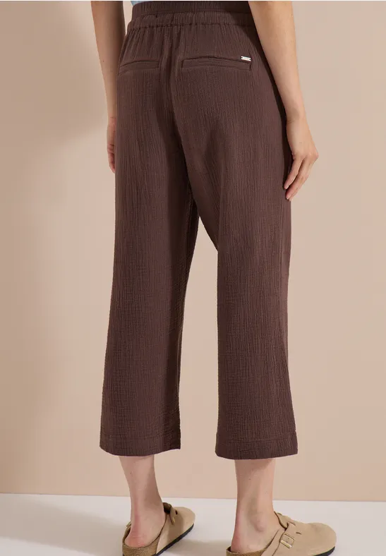 Braune, knöchellange, weite Hose mit elastischem Bund, Rückansicht, getragen mit beigen Pantoletten.