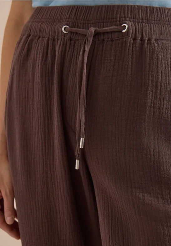 Nahaufnahme einer braunen, texturierten Hose mit elastischem Bund und Kordelzug mit silbernen Endkappen.