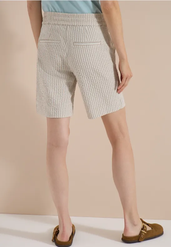 Person in hoch taillierten, gestreiften Bermudashorts, von hinten fotografiert, mit Mokassins.