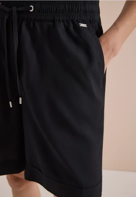 Zwarte sportshort tot op de knie met elastische taille, trekkoord en steekzakken aan de zijkant.