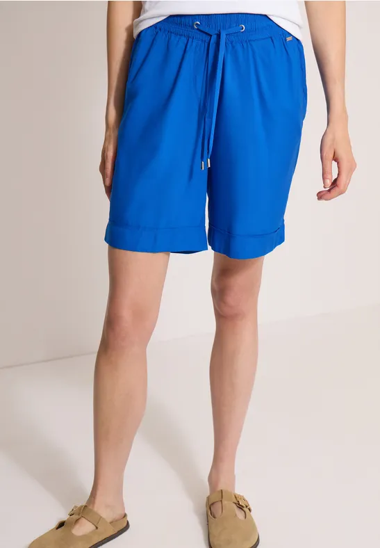 Eine Person trägt knielange, leuchtend blaue Shorts mit Kordelzug und beige Sandalen.