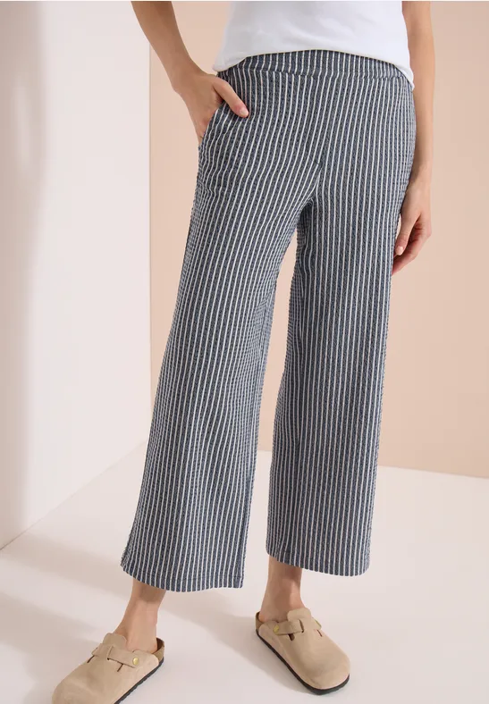 Wijde, enkellange broek in marineblauw met fijne witte strepen, zijzakken, gecombineerd met beige muiltjes.