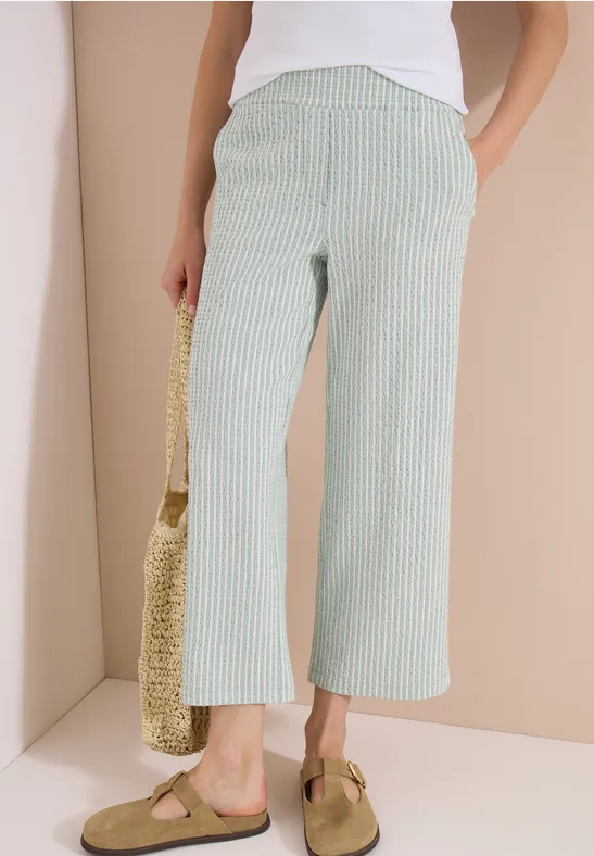 Dames culotte met groen-witte strepen, gecombineerd met een wit topje, een strooien tas en muiltjes.