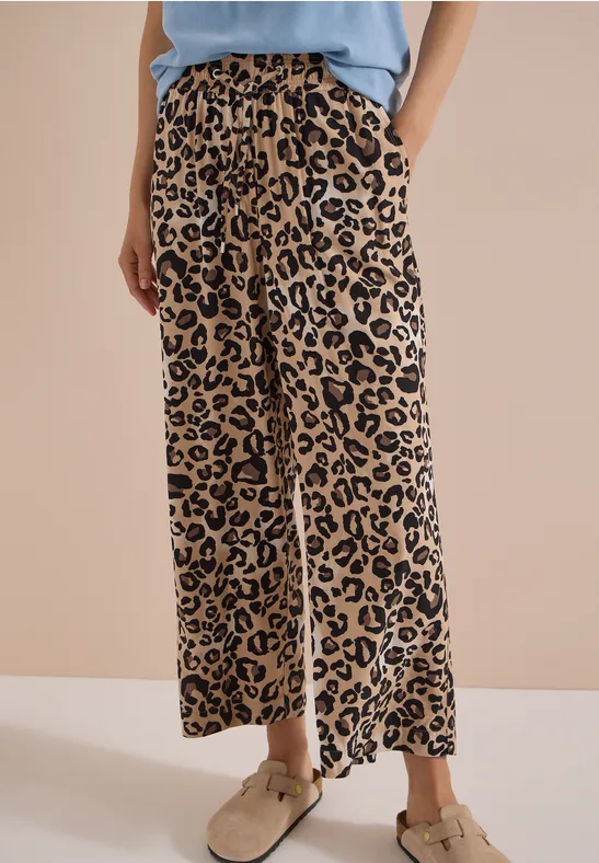 Benen in wijde beige-zwart luipaardprint broek, gecombineerd met beige schoenen en licht topje.