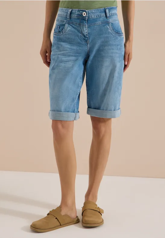Persoon draagt lichtblauwe jeansbermuda en beige sandalen voor een neutrale achtergrond.