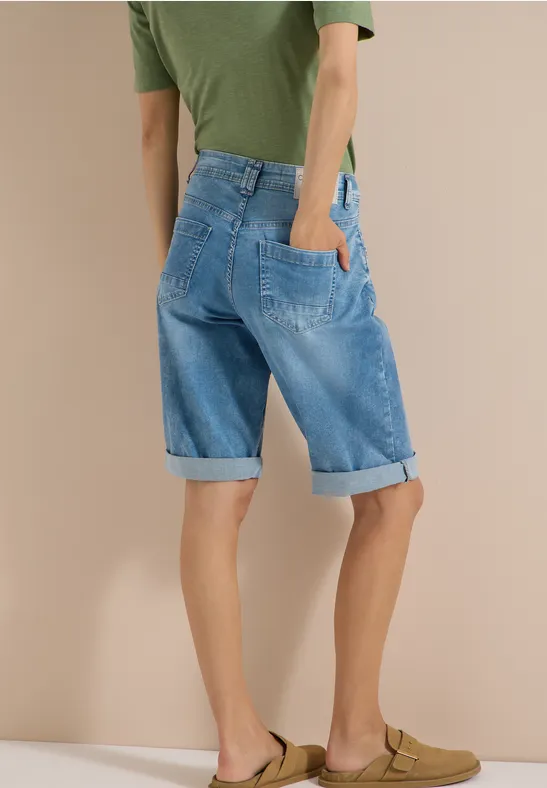 Achteraanzicht van persoon in groen T-shirt, opgerolde blauwe denim bermuda en bruine sandalen.