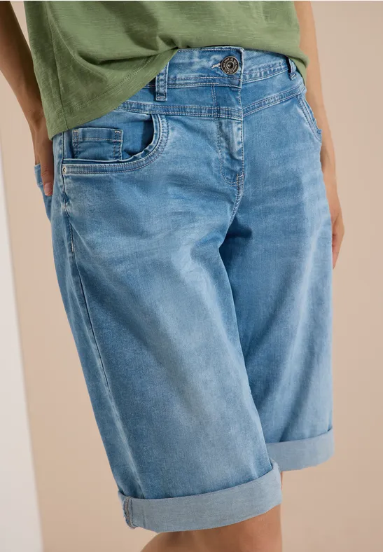 Persoon draagt groen T-shirt en lichtblauwe denim bermuda met omgeslagen pijpen.