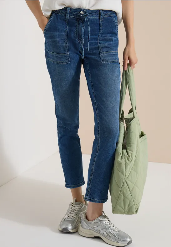 Hüfthohe, dunkelblaue Jeans mit Bündchen, grauen Sneakern und einer hellgrünen, gesteppte Tasche.
