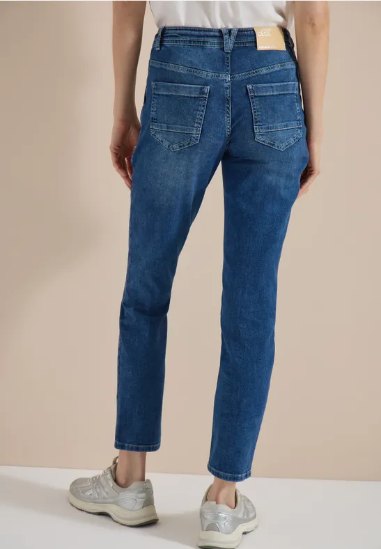 Rückansicht einer Person in blauen Jeans und grauen Sneakern vor neutralem Hintergrund.