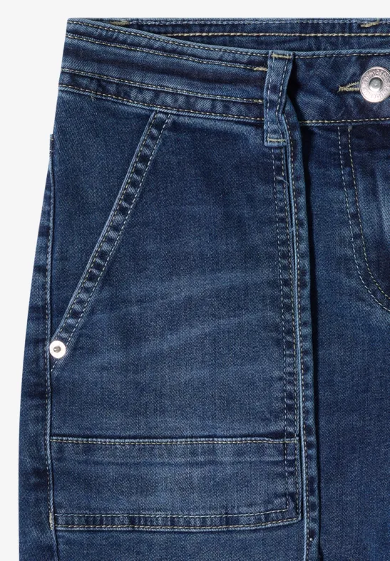 Nahaufnahme einer blauen Jeanshose mit Fronttasche, Gürtelschlaufen und silbernem Nieten-Detail.