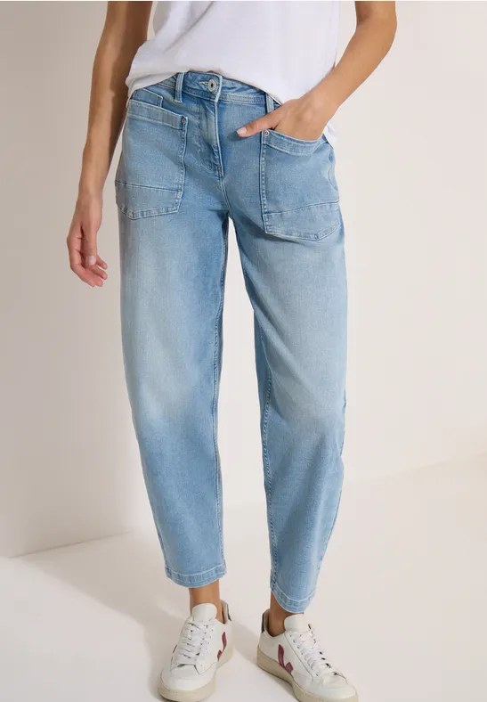 Eine Person trägt helle High-Waist-Jeans und weiße Sneaker vor neutralem Hintergrund.