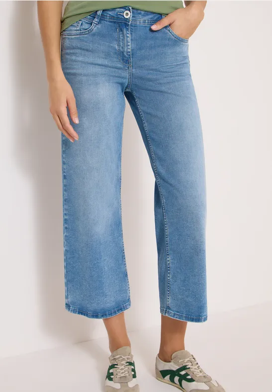 Helle, knöchellange Jeans mit weitem Bein, kombiniert mit weißen Sneakern mit grünen Akzenten.