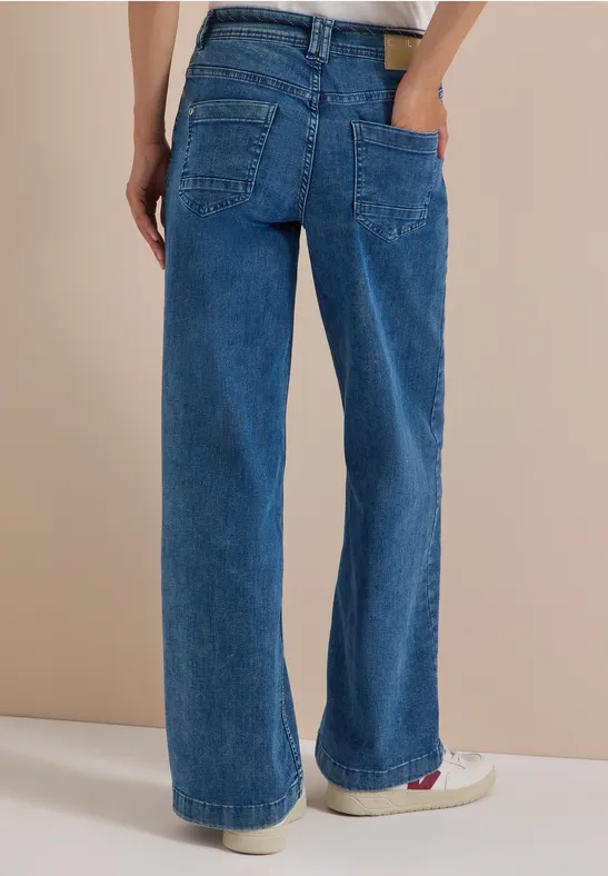 Rückansicht einer Person in weiten, blauen Jeanshosen aus Denim mit aufgesetzten Taschen und geradem Bein.