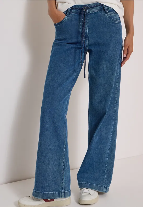 Person trägt blaue, weite Jeans mit hohem Bund und weißen Sneakers.