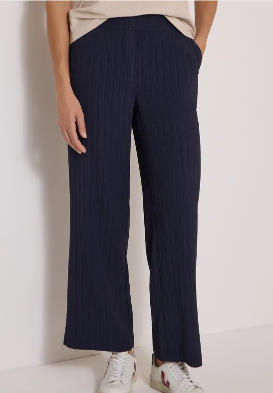 Frau trägt marineblaue, gestreifte, weit geschnittene Hose mit Taschen und weißen Sneakers.