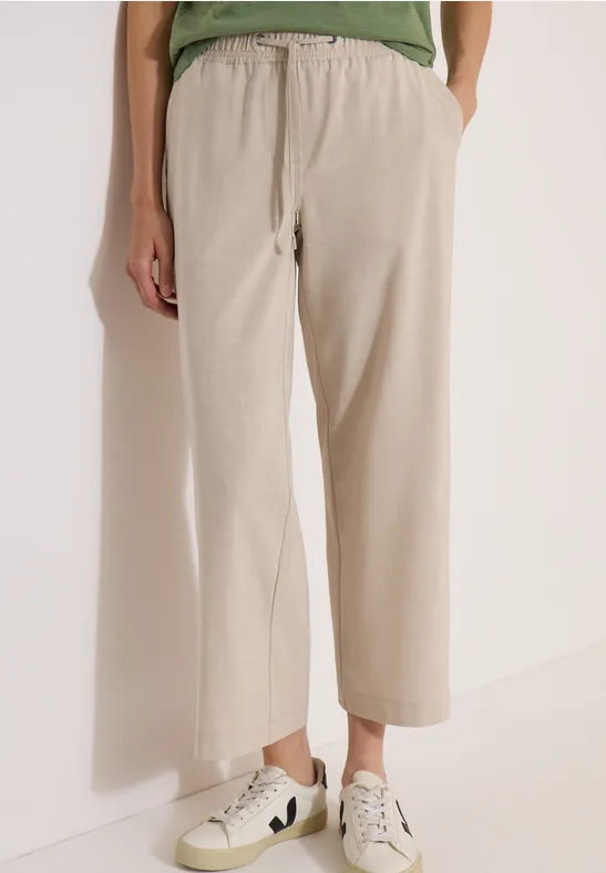 Beige wijde broek tot op de enkels, van lichte stof, gecombineerd met lichte sneakers.