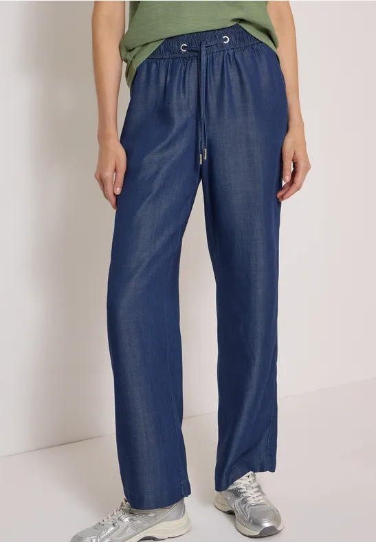 Weit geschnittene, hoch taillierte, dunkelblaue Hose mit Tunnelzug und silbernen Sneakern.