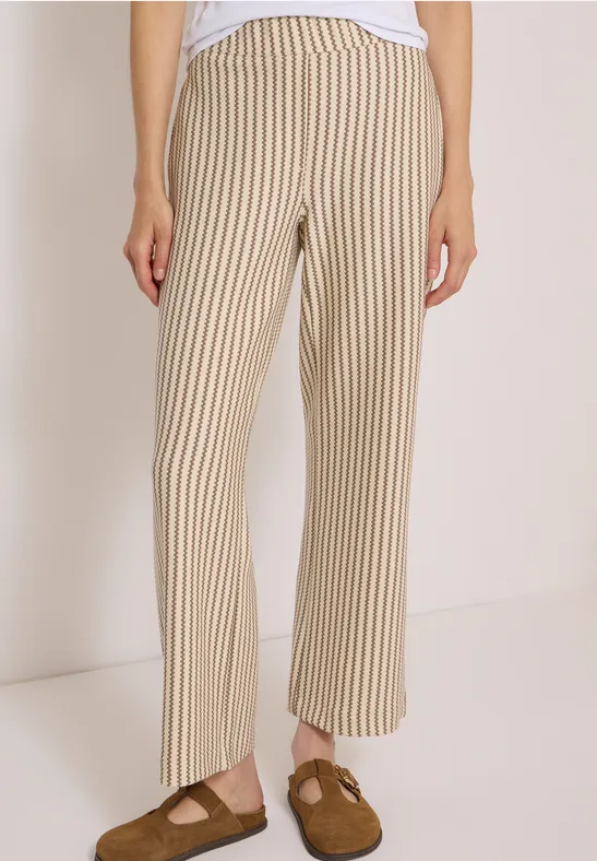 Beige-weiß gestreifte, weit geschnittene Hose mit braunen Sandalen vor hellem Hintergrund.