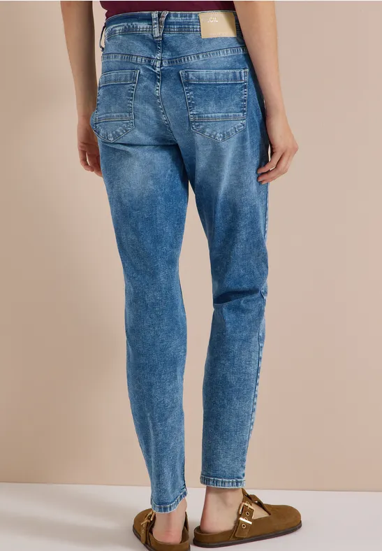 Person trägt hoch geschnittene, stonewashed blaue Mom-Jeans und braune Sandalen.