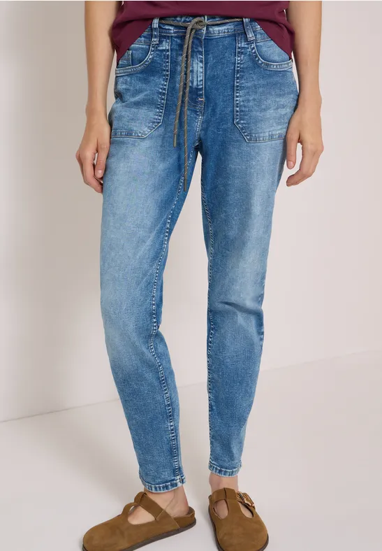 Eine Person trägt lässige blaue Jeans mit Tunnelzugtaillenband und Taschen, kombiniert mit Sandaletten.