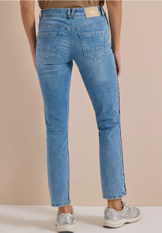 Hinteransicht einer Person in hellblauen Jeans und Sneakers vor beigem Hintergrund.