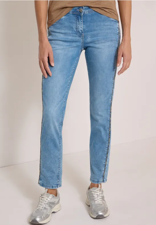 Person in hellblauen Jeans und silbernen Sneakers vor einfarbigem Hintergrund.