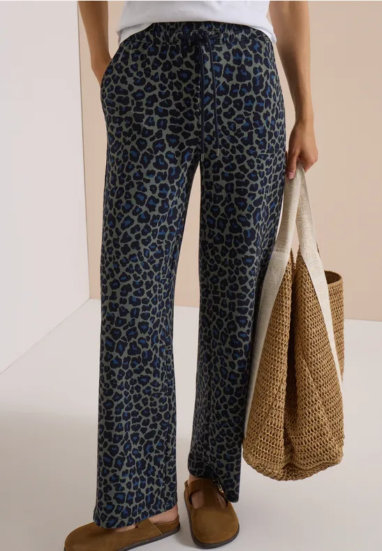 Pantalon ample à motif bleu-noir, chemise blanche, sac en osier et chaussures marron.